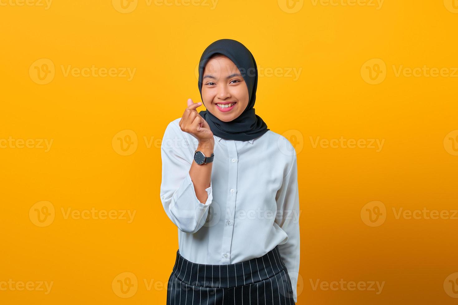Sonriente joven mujer asiática mostrando signo de gesto de amor sobre fondo amarillo foto