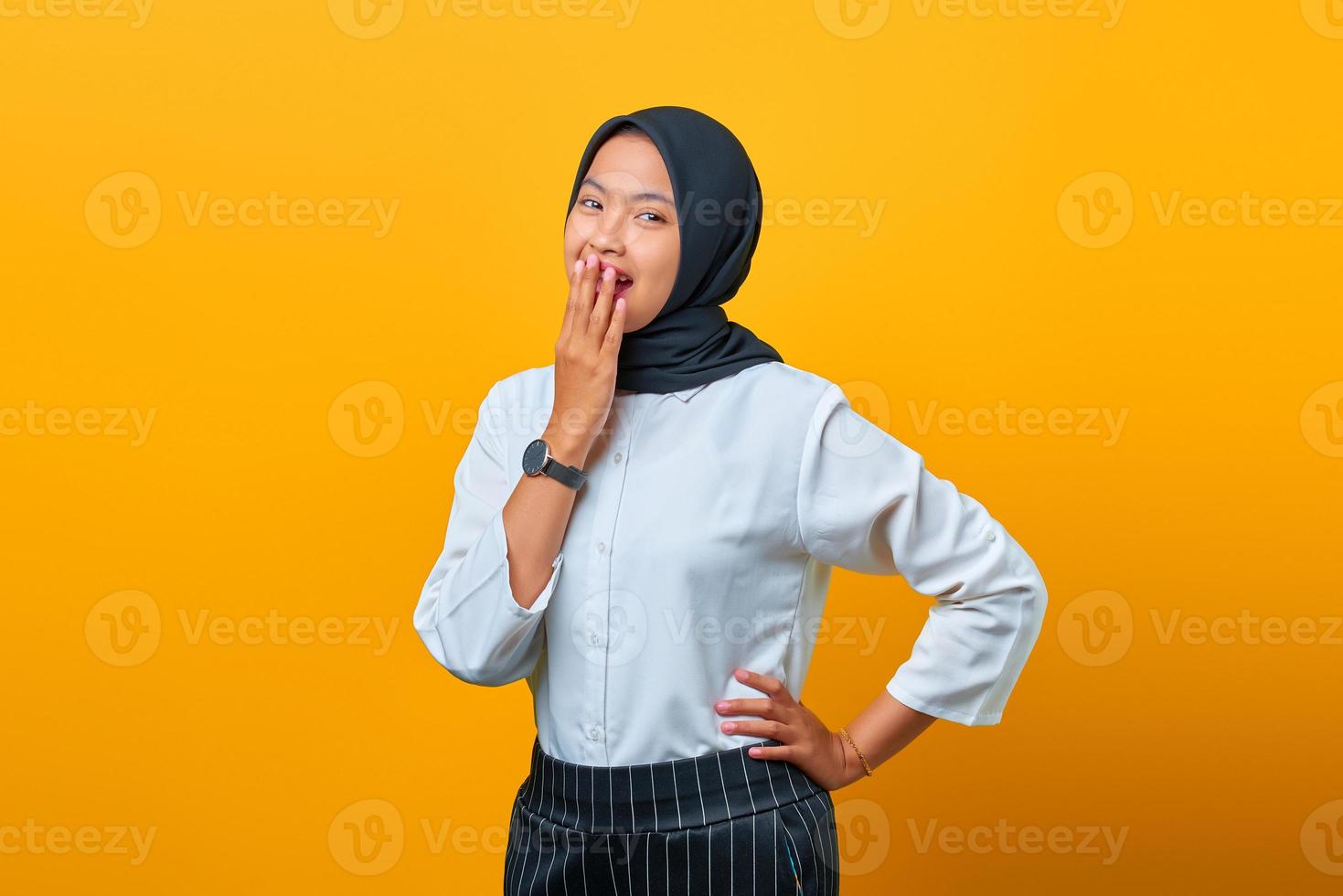 Feliz joven mujer asiática reír y cubrirse la boca con la mano aislada sobre fondo amarillo foto