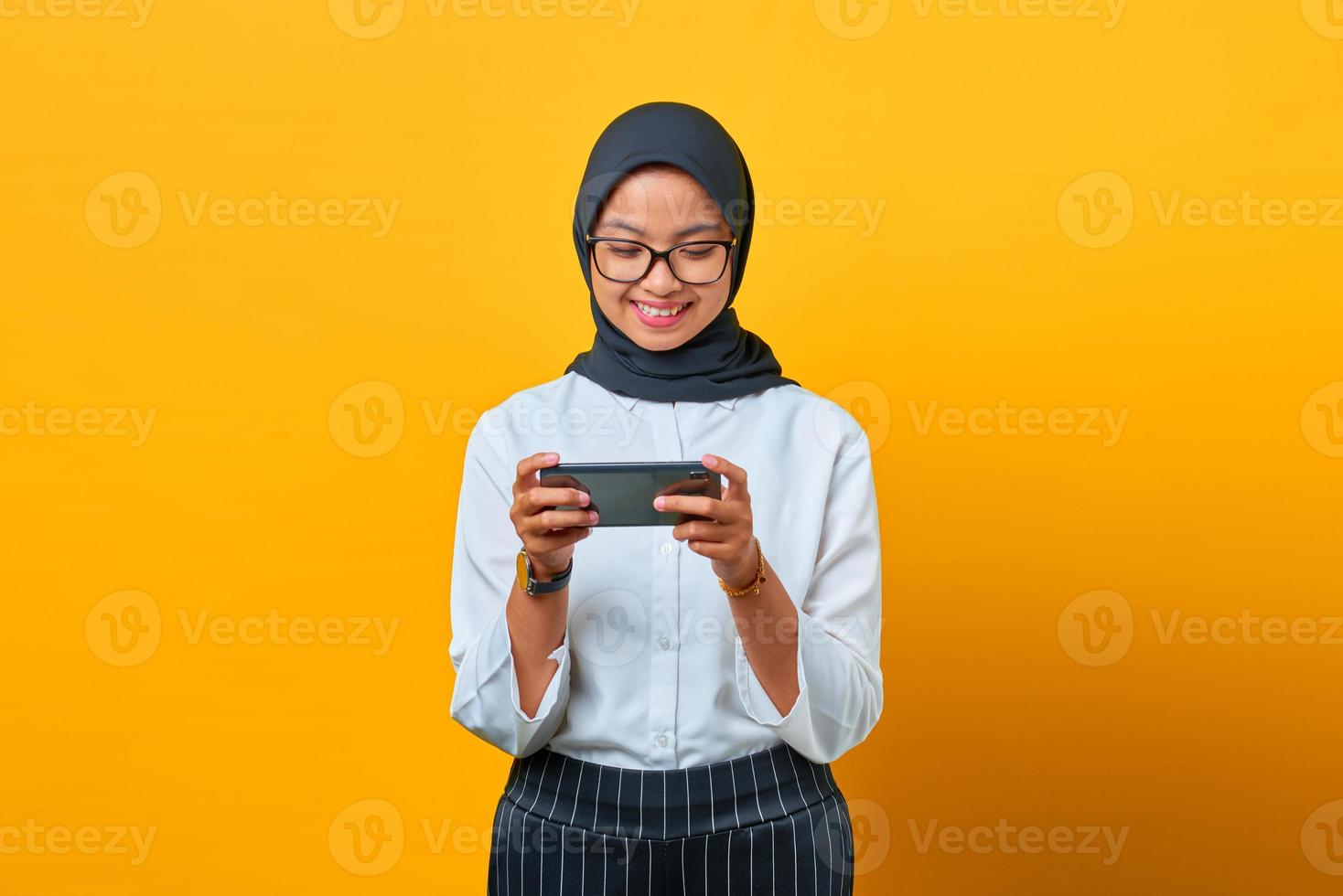 Feliz joven mujer asiática con teléfono móvil jugando sobre fondo amarillo foto