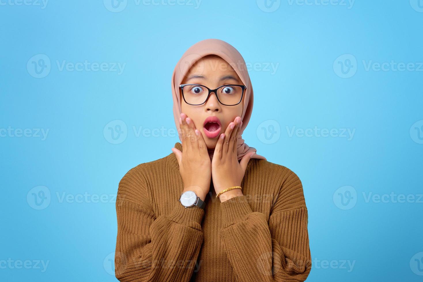 Retrato de mujer asiática joven sorprendida con la boca abierta sobre fondo azul. foto