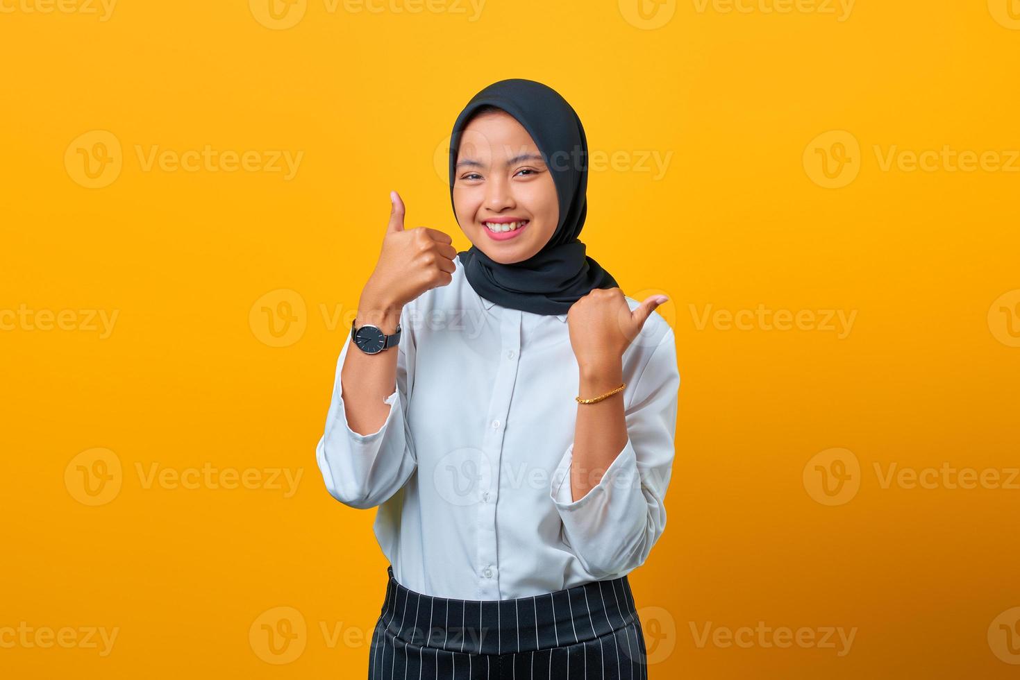 Sonriente hermosa mujer asiática haciendo pulgar hacia arriba aislado sobre fondo amarillo foto