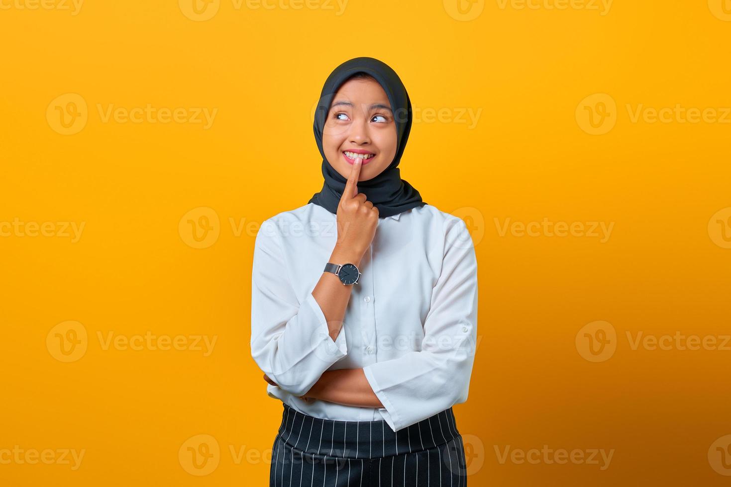 Emocionada joven asiática tocando los labios y teniendo ideas sobre fondo amarillo foto