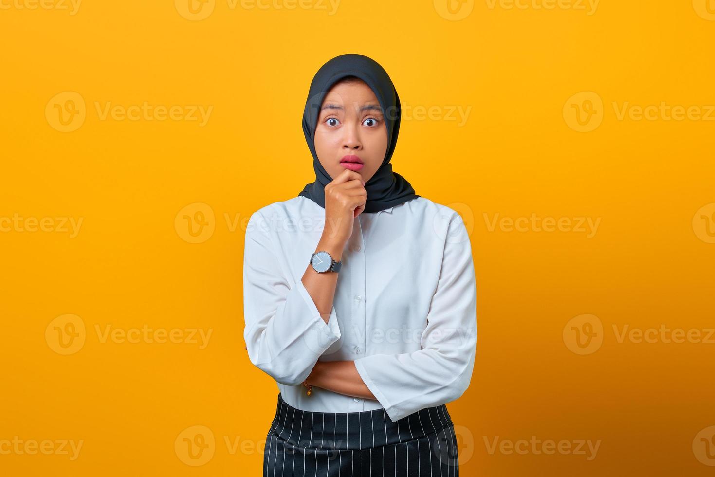 Retrato de mujer asiática hermosa nerviosa parece preocupada y con la mano en los labios sobre fondo amarillo foto