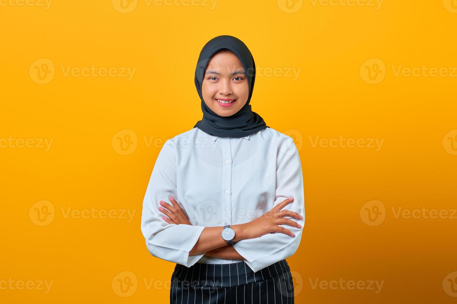 Happy beautiful Asian woman standing with crossed arm and looking camera on yellow background photo