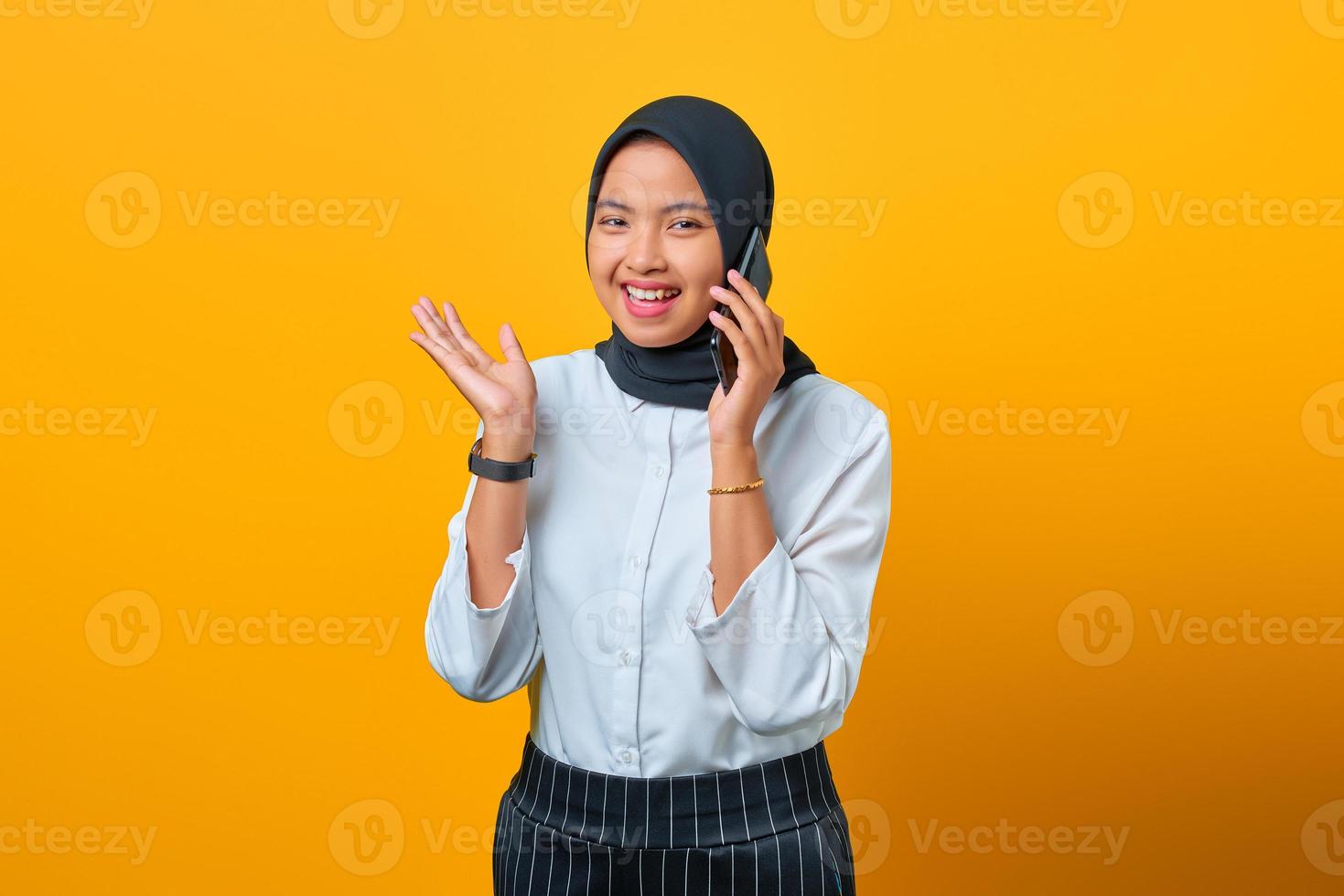 Sonriente joven mujer asiática hablando por teléfono inteligente aislado sobre fondo amarillo foto