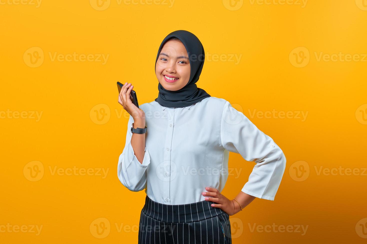 Portrait of happy young Asian woman celebrates with a mobile phone on yellow background photo