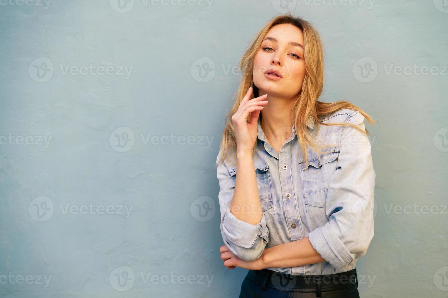 mujer rubia vestida con camisa de mezclilla y falda de cuero negro de pie en la calle. foto