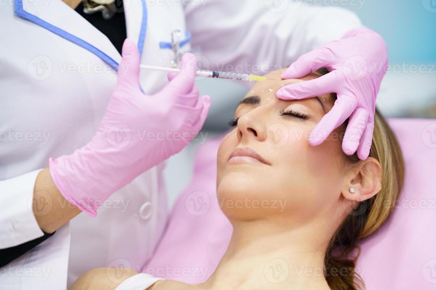 Aesthetic doctor injecting botox into the forehead of her middle-aged patient. photo