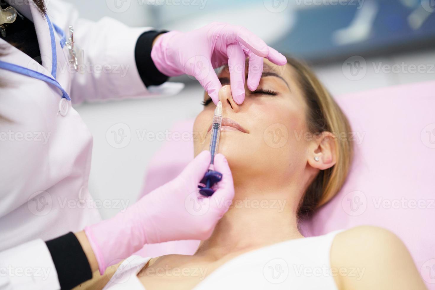 Doctor performing rhinoplasty by injection of hyaluronic acid in the nose of his patient. photo