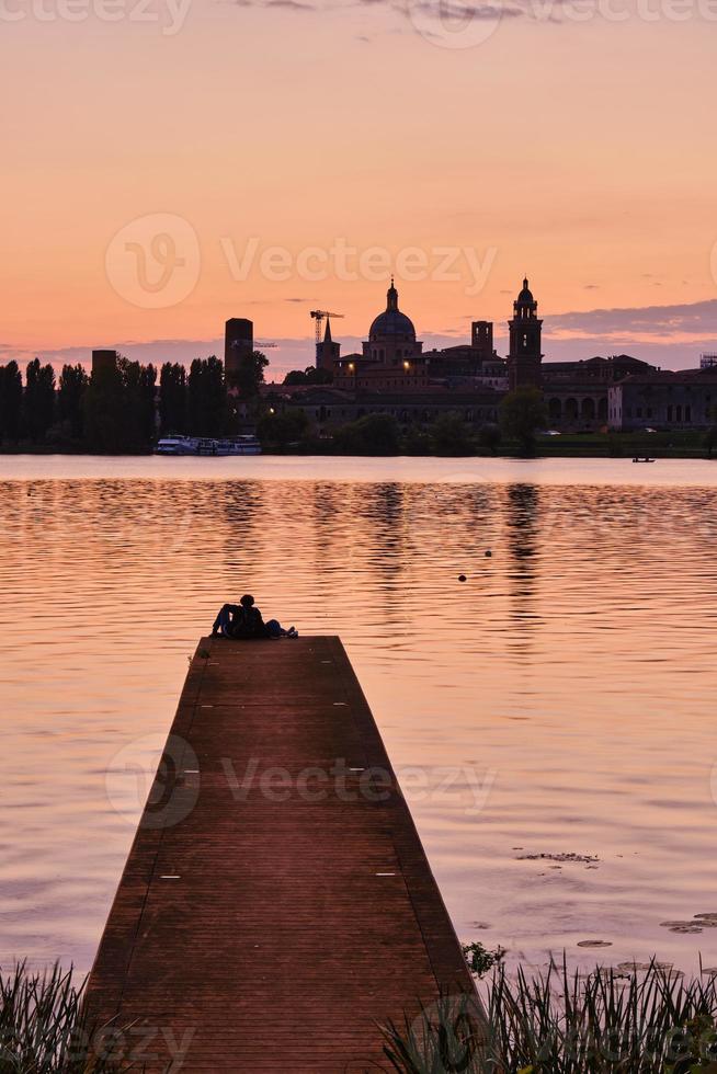 Couple sitting on pier looking at the sunset and the city skyline photo