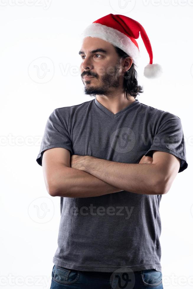 Retrato de hombre latino con sombrero de navidad mirando hacia el lado con los brazos cruzados. Fondo blanco foto