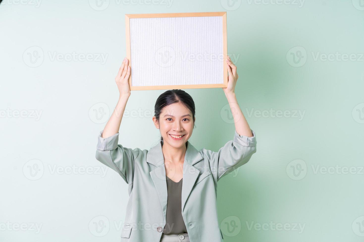 Young Asian businesswoman holding white board on green background photo