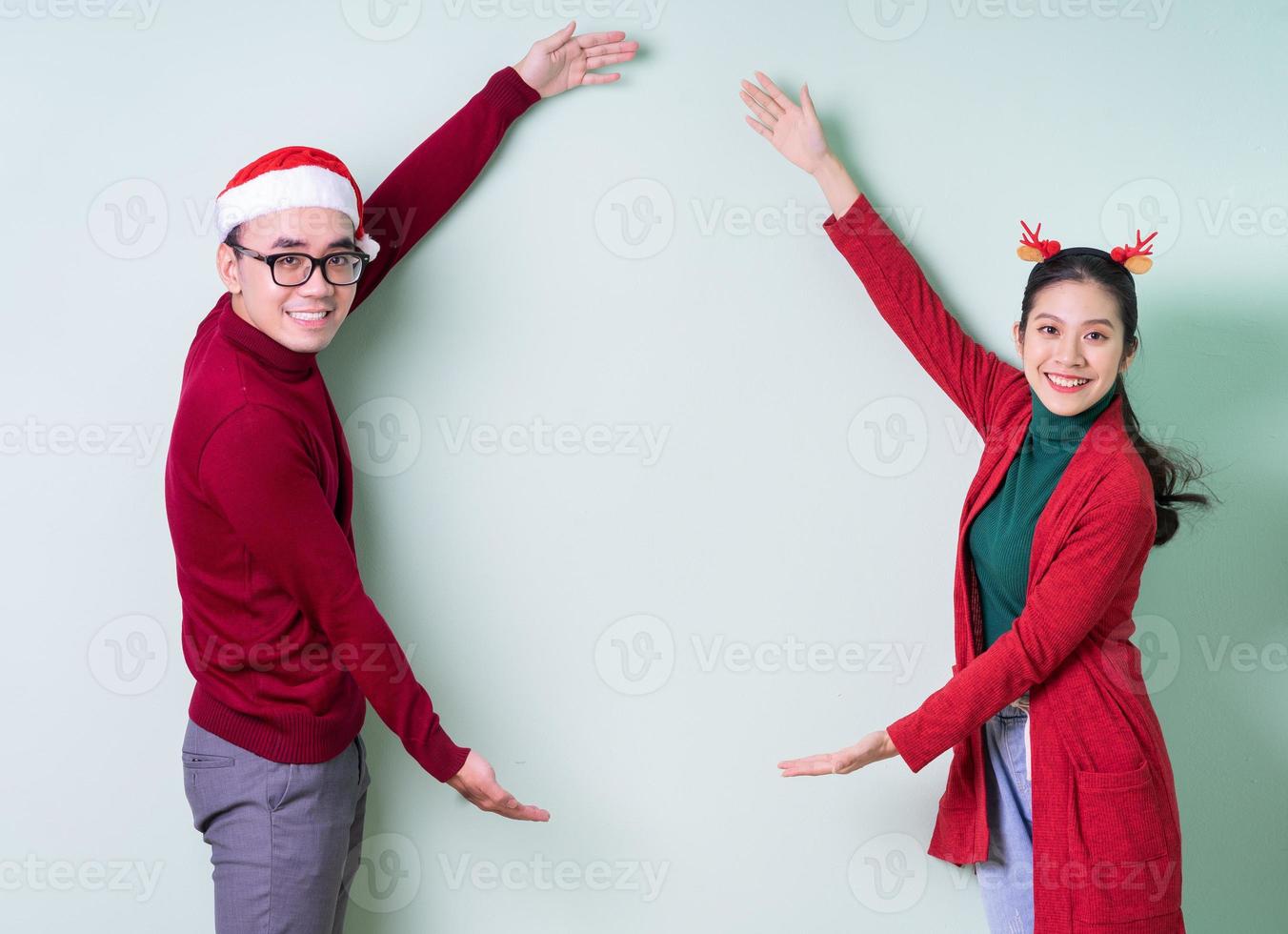 Young Asian couple posing on green background with christmas concept photo