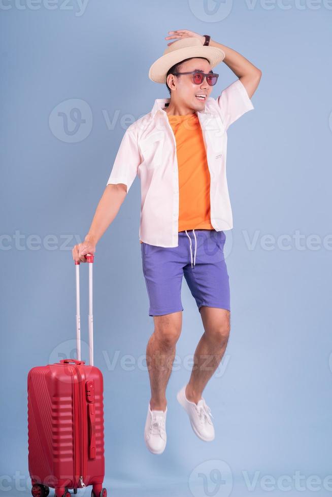 Young Asian man holding red suitcase on blue background photo