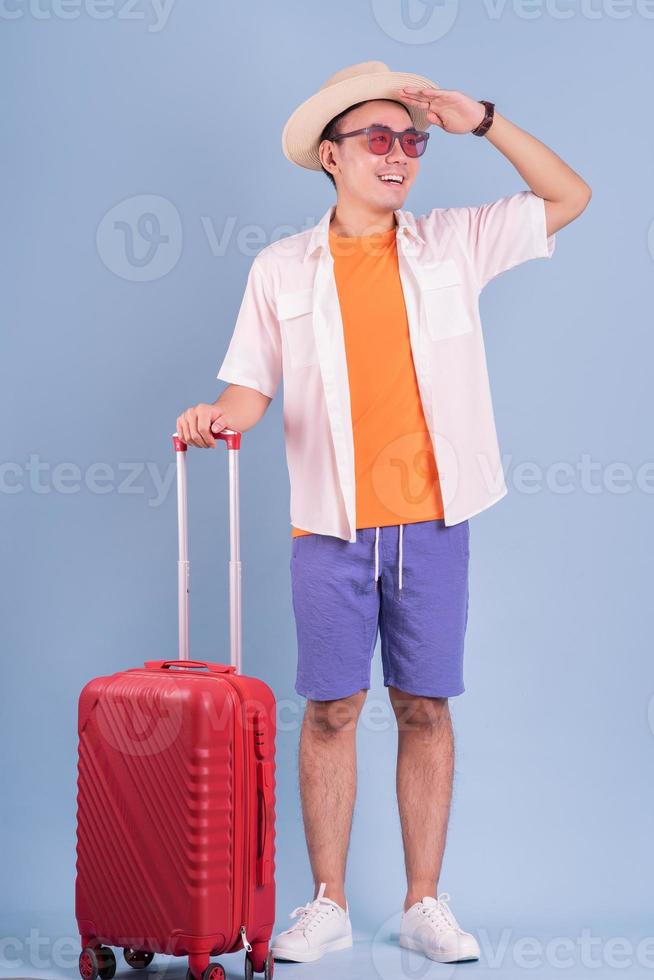 Young Asian man holding red suitcase on blue background photo