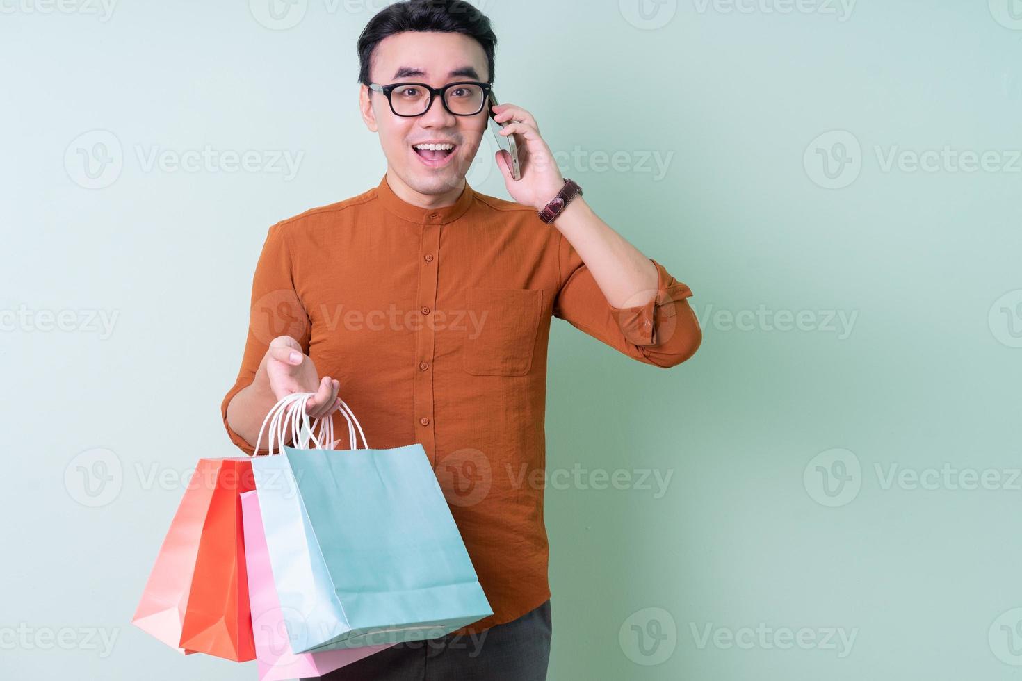Young Asian man holding shopping bag on green background photo