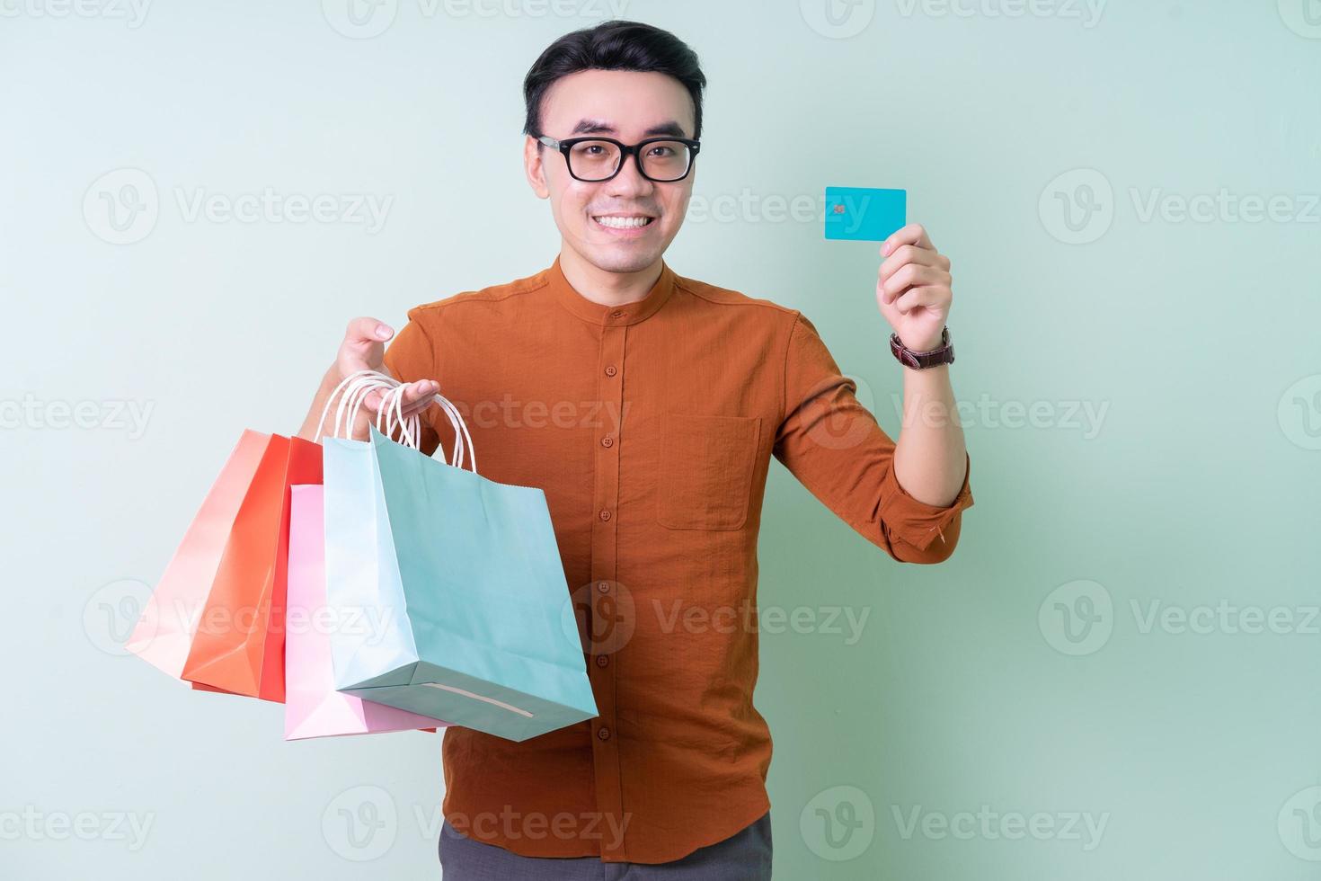 Young Asian man holding shopping bag on green background photo