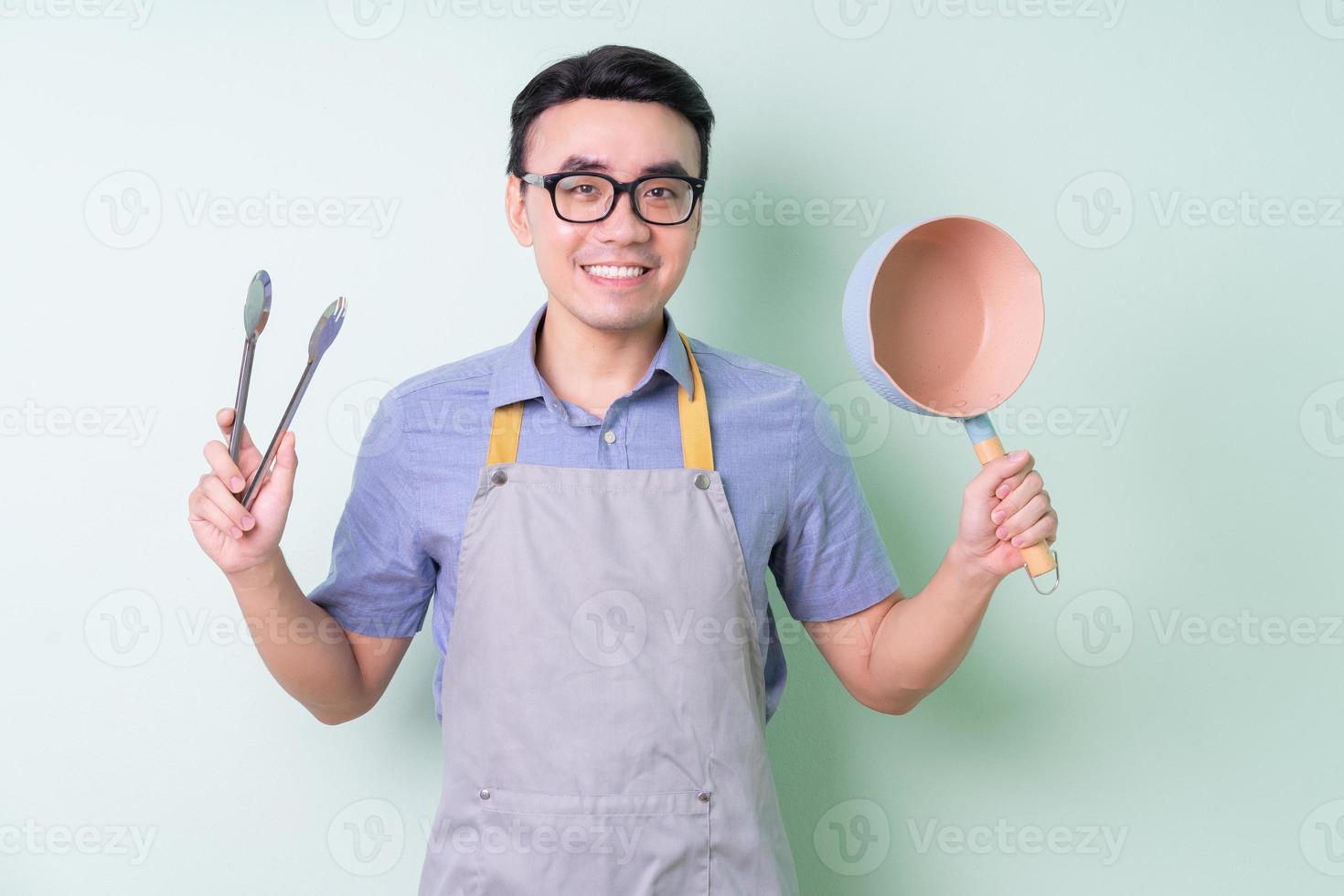 Young Asian man wearing apron posing on green background photo