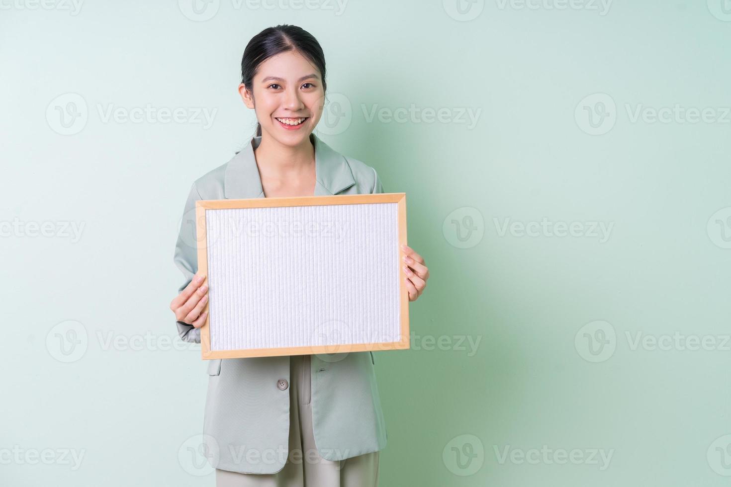 Young Asian businesswoman holding white board on green background photo