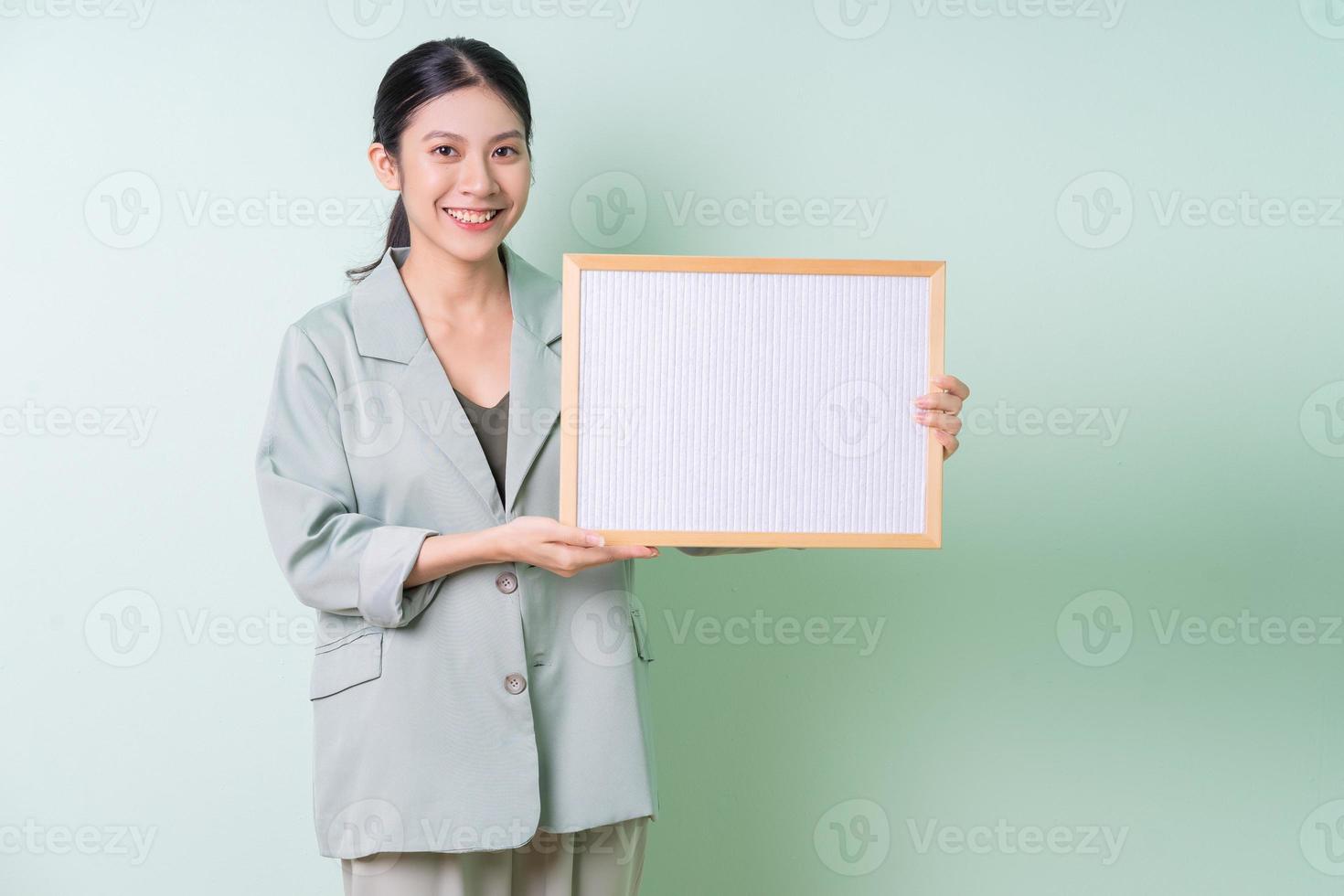 Young Asian businesswoman holding white board on green background photo