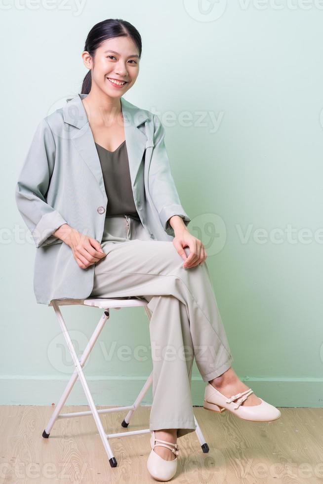 Joven empresaria asiática sentada en una silla sobre fondo verde foto