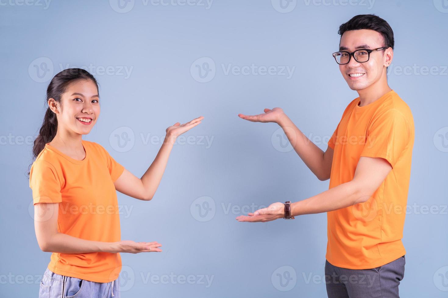 Joven pareja asiática vistiendo camiseta naranja sobre fondo azul. foto