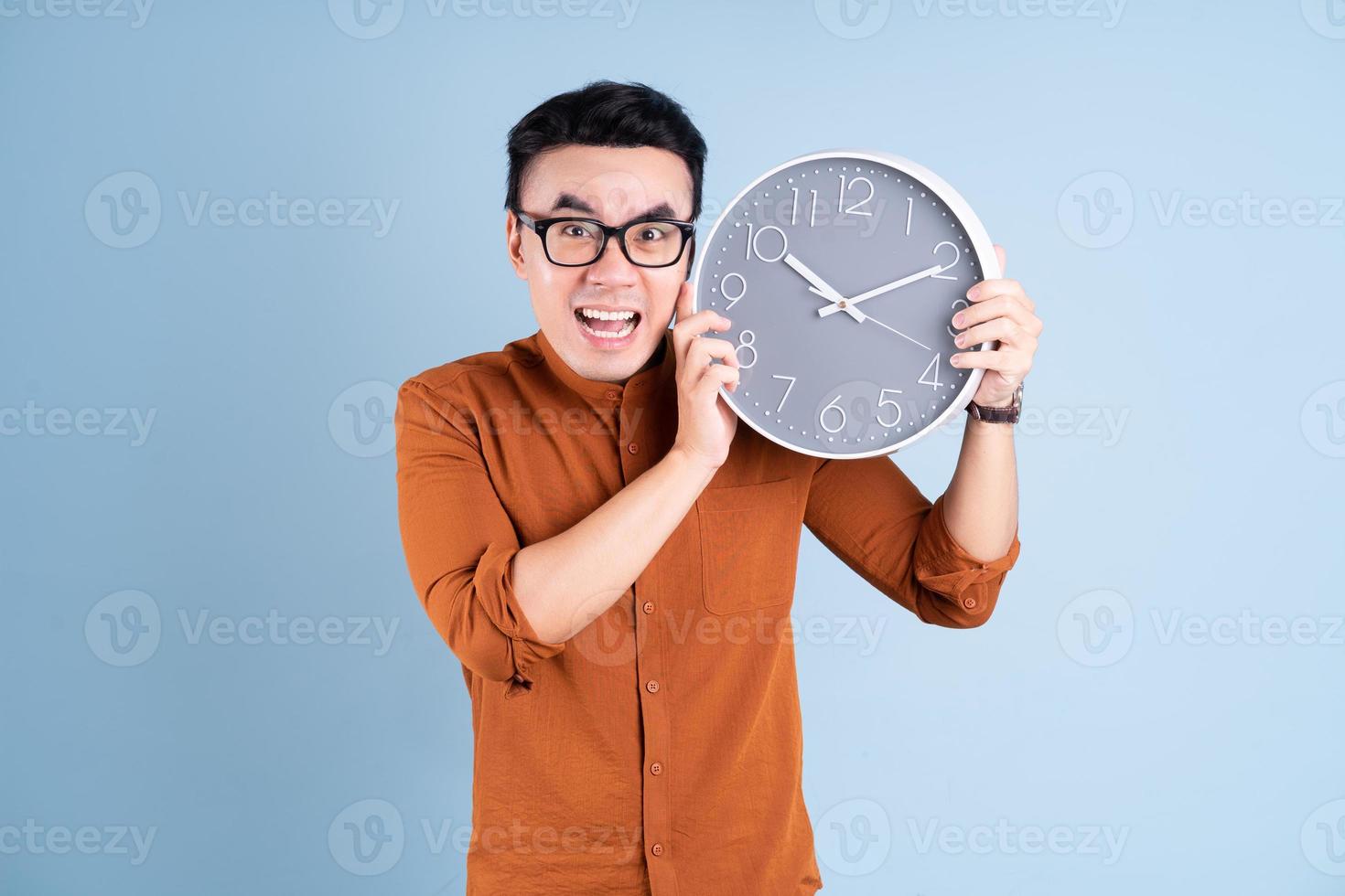 Young Asian man holding clock on blue background photo