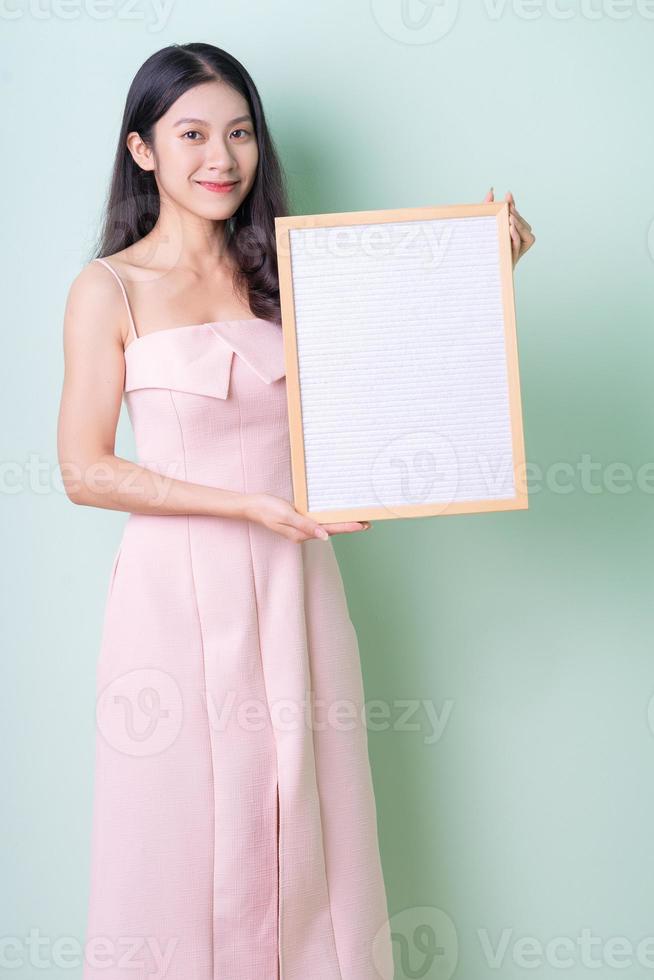 Beautiful young Asian woman holding white board on green background photo