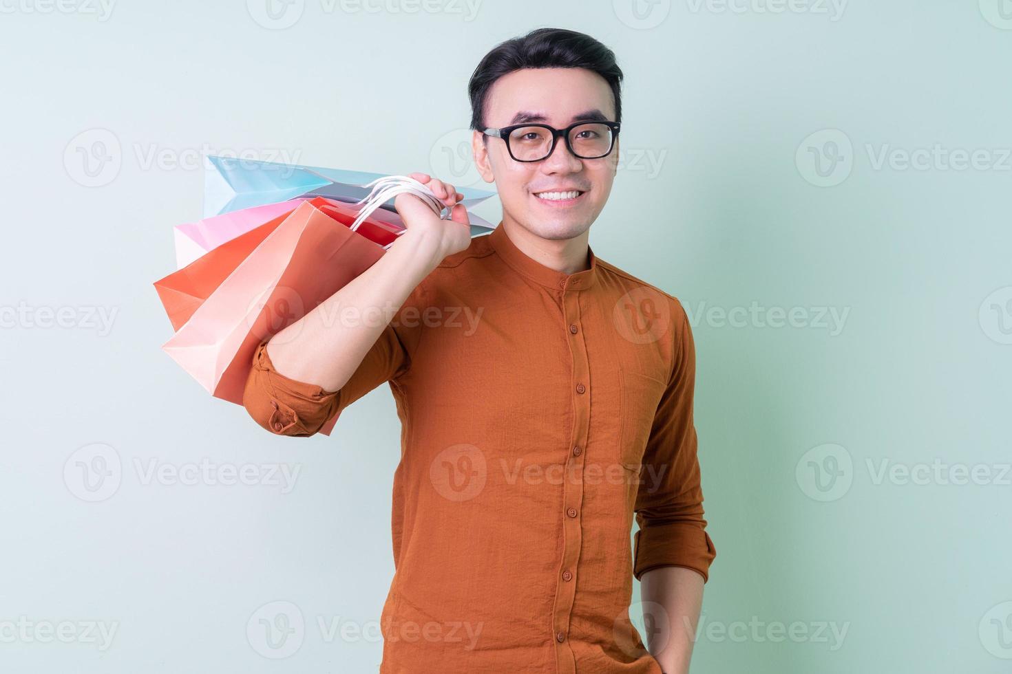 Young Asian man holding shopping bag on green background photo