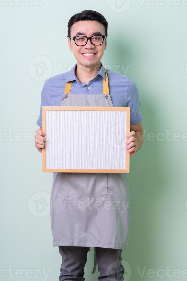 joven, asiático, hombre, llevando, delantal, posar, en, fondo verde foto