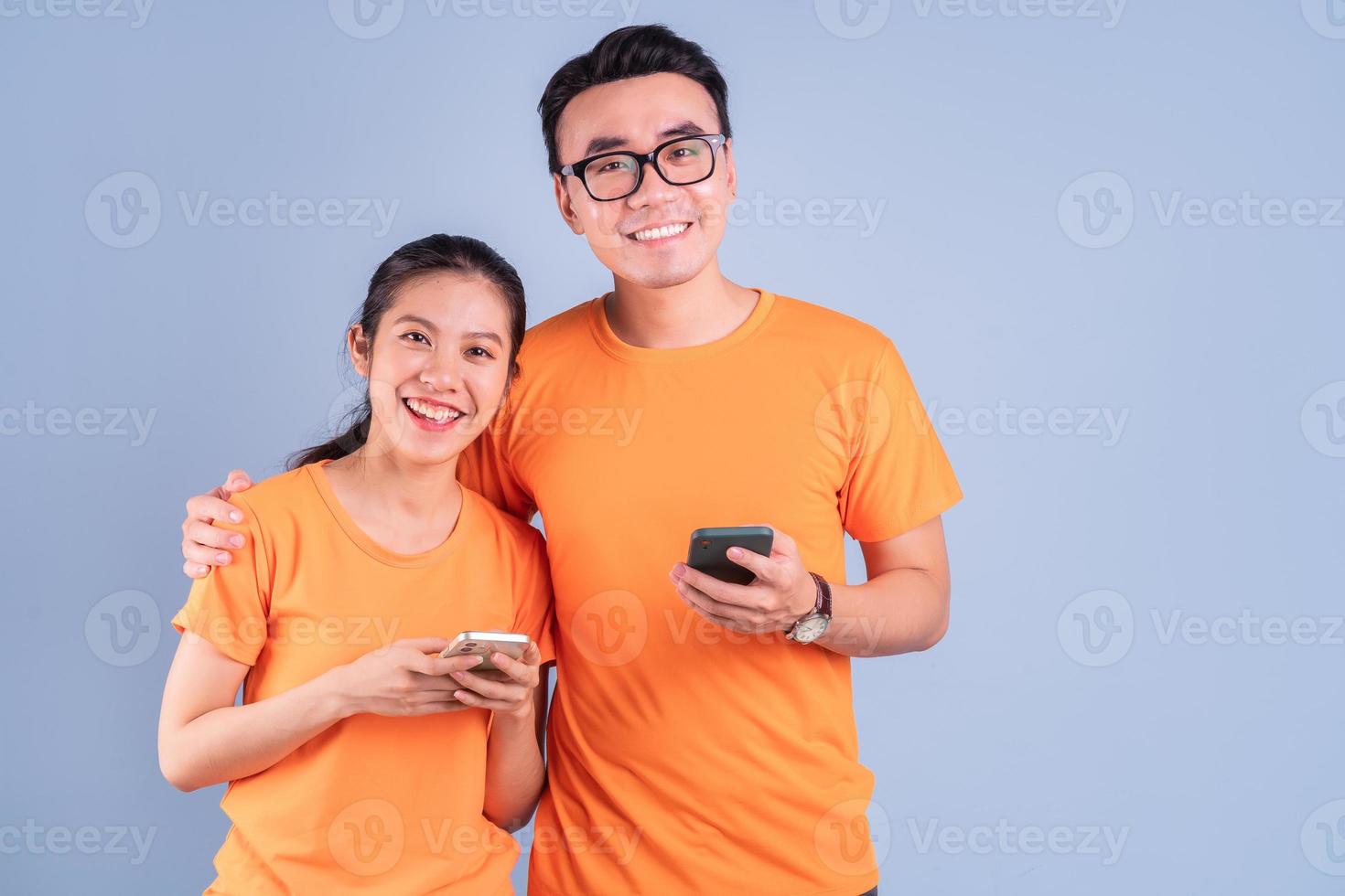 Joven pareja asiática vistiendo camiseta naranja sobre fondo azul. foto