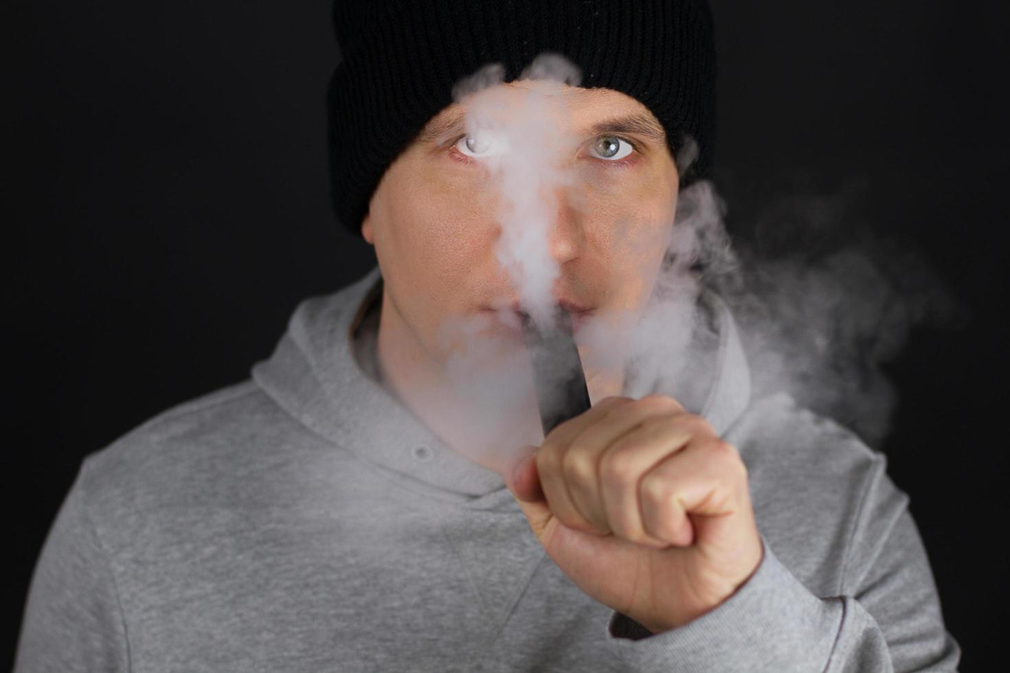 Unrecognizable man in the cloud of vape smoke. Guy smoking e-cigarette to quit tobacco. Vapor and alternative nicotine free smoking concept, copy space selective focus photo