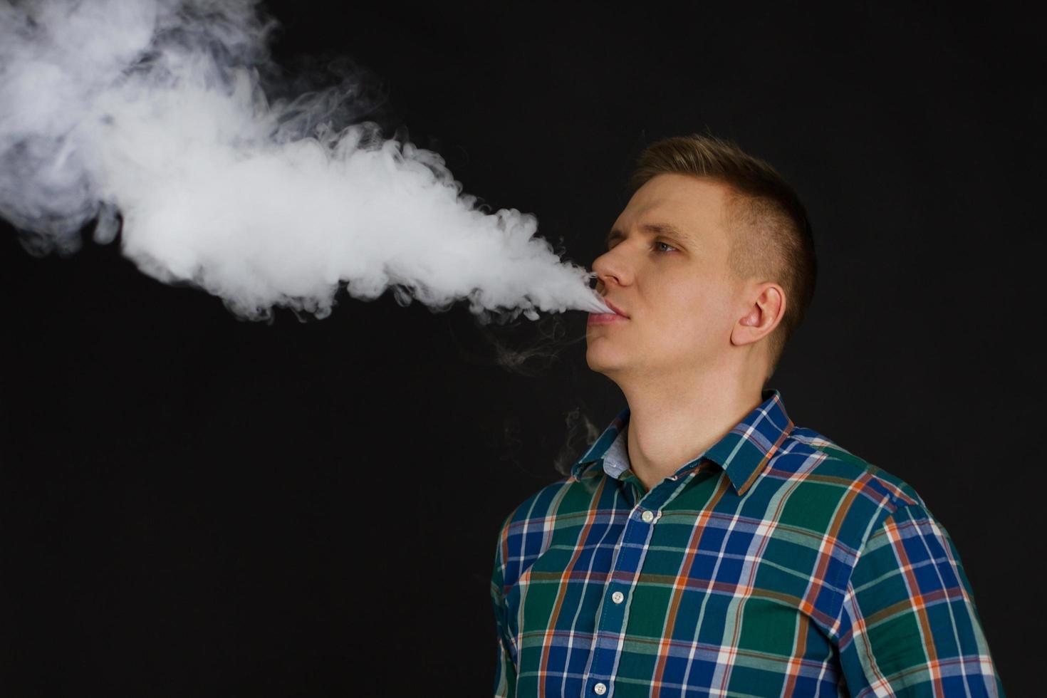 Hombre blanco en camisa chekered vaping y libera una nube de vapor enfoque selectivo foto