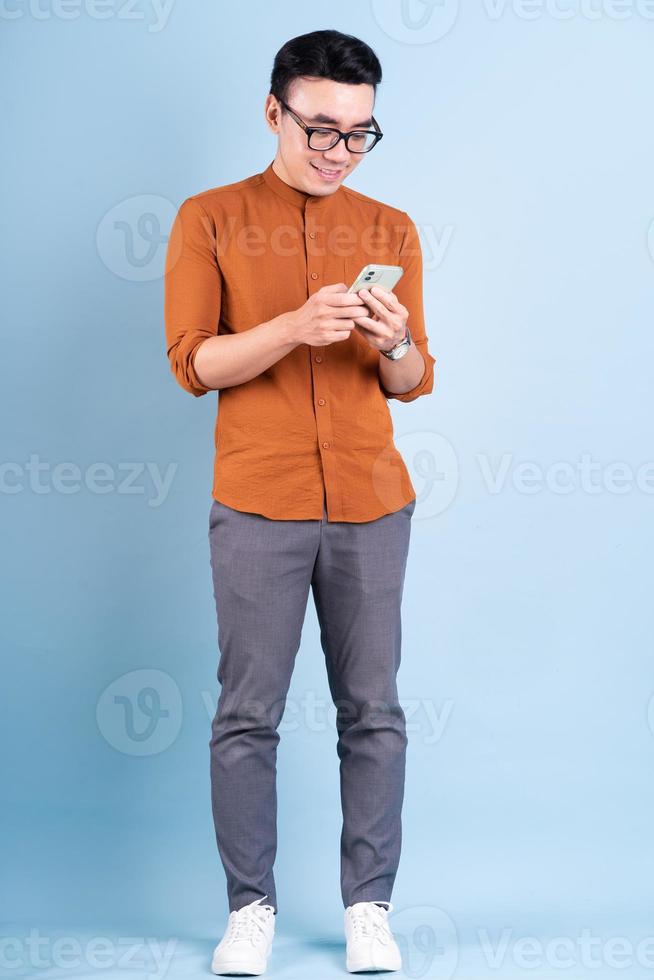 Young Asian man using smartphone on blue background photo