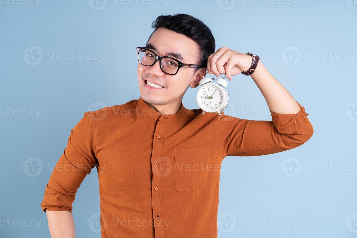 Young Asian man holding clock on blue background photo