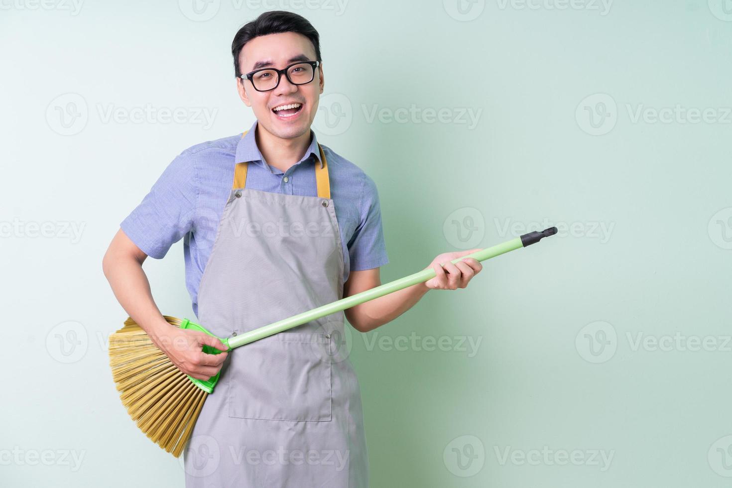 joven, asiático, hombre, llevando, delantal, posar, en, fondo verde foto