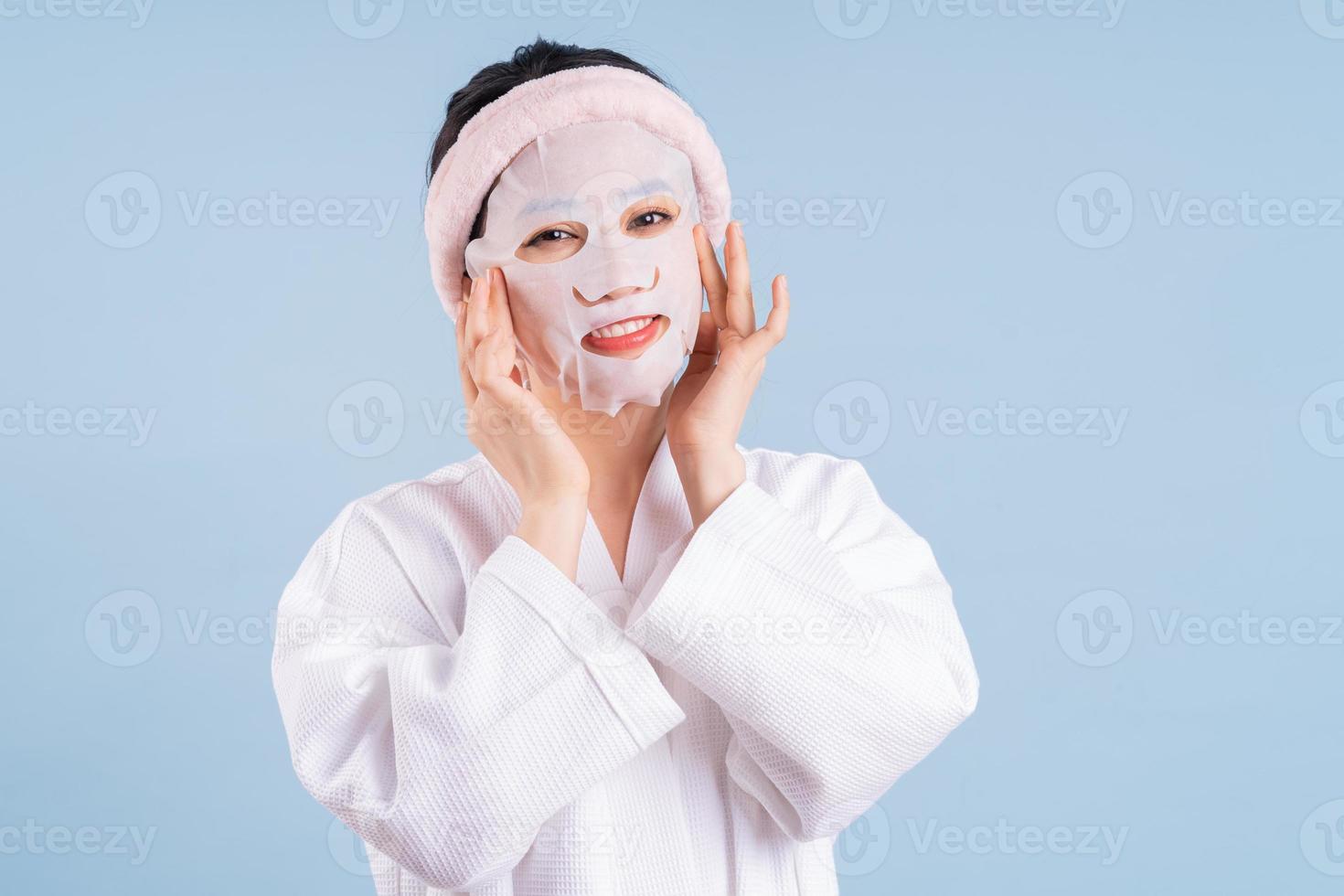 Joven mujer asiática vistiendo albornoz sobre fondo azul. foto