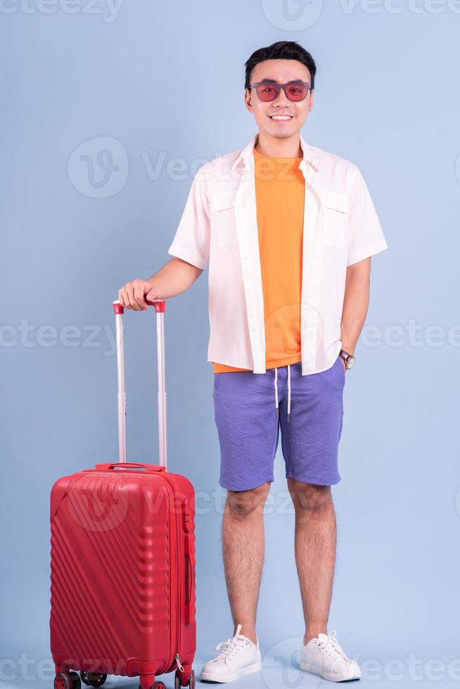 Young Asian man holding red suitcase on blue background photo