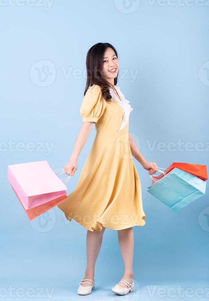 Beautiful young Asian woman holding shopping bag on blue background photo