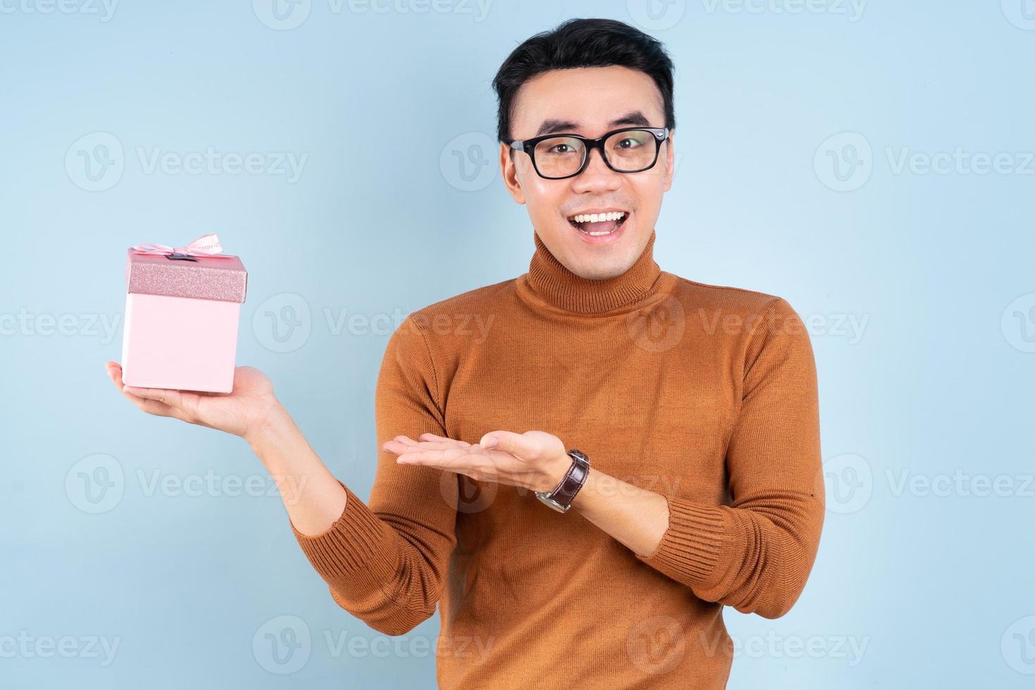 Hombre asiático con caja de regalo rosa sobre fondo azul. foto
