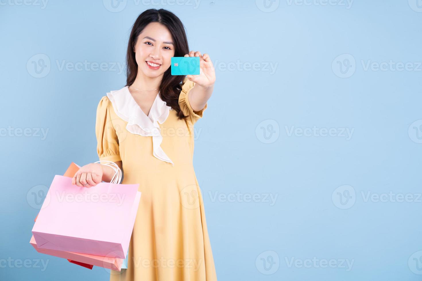 Beautiful young Asian woman holding shopping bag on blue background photo