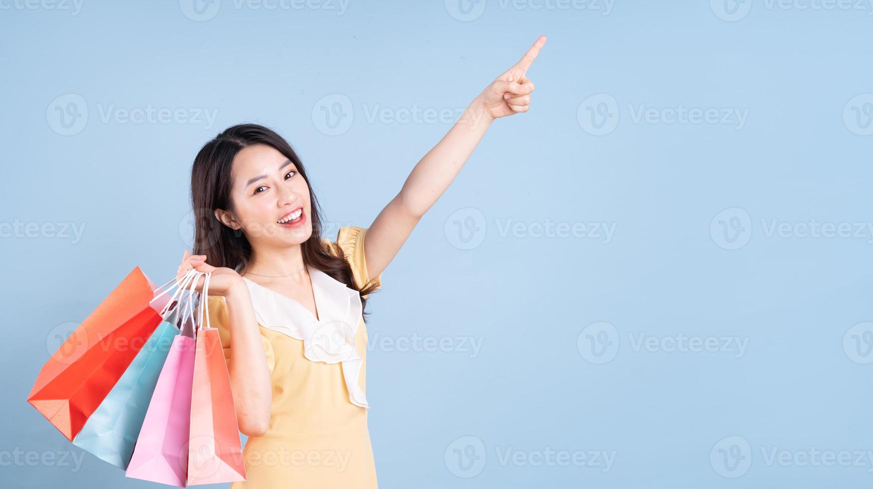 Beautiful young Asian woman holding shopping bag on blue background photo