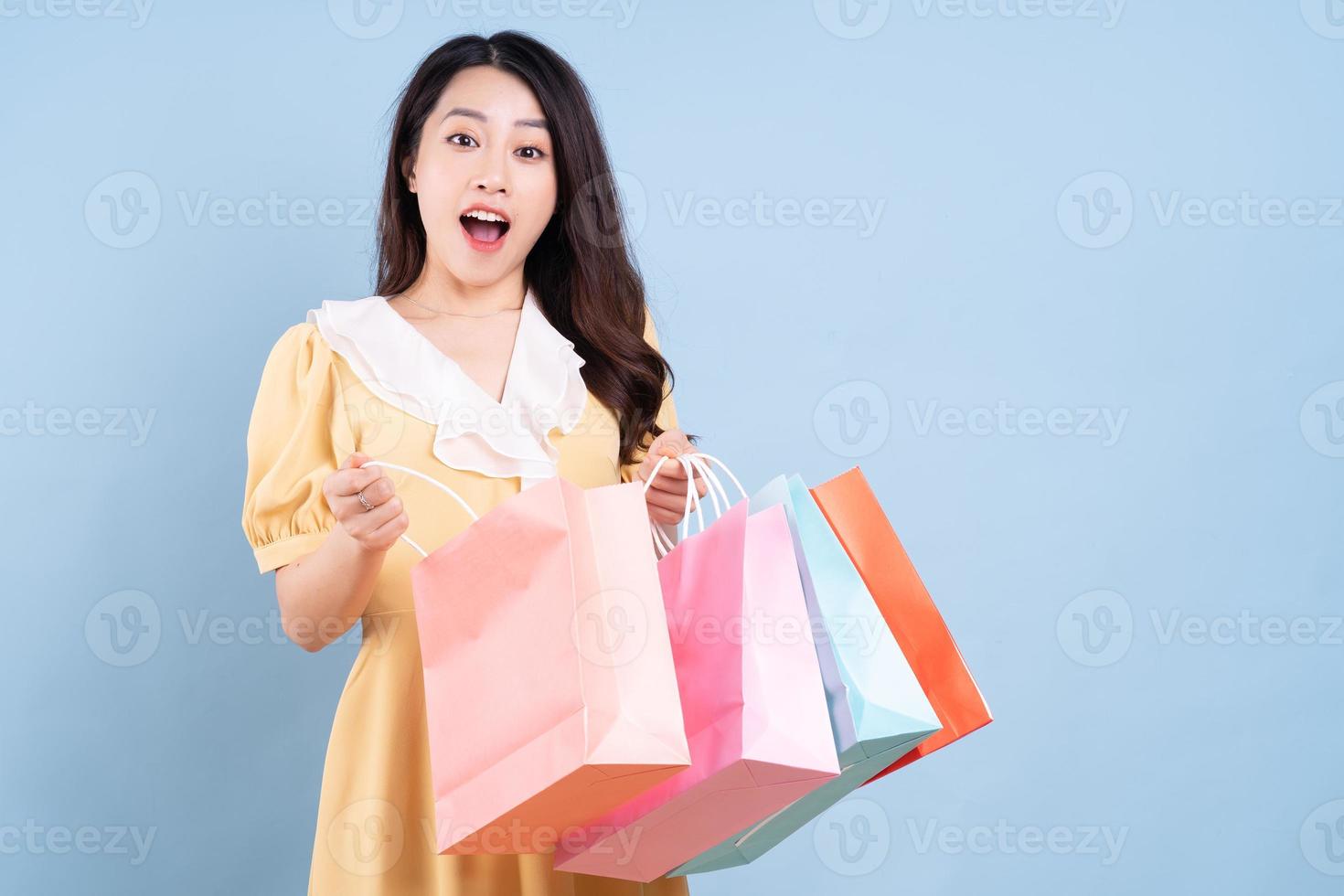 Beautiful young Asian woman holding shopping bag on blue background photo