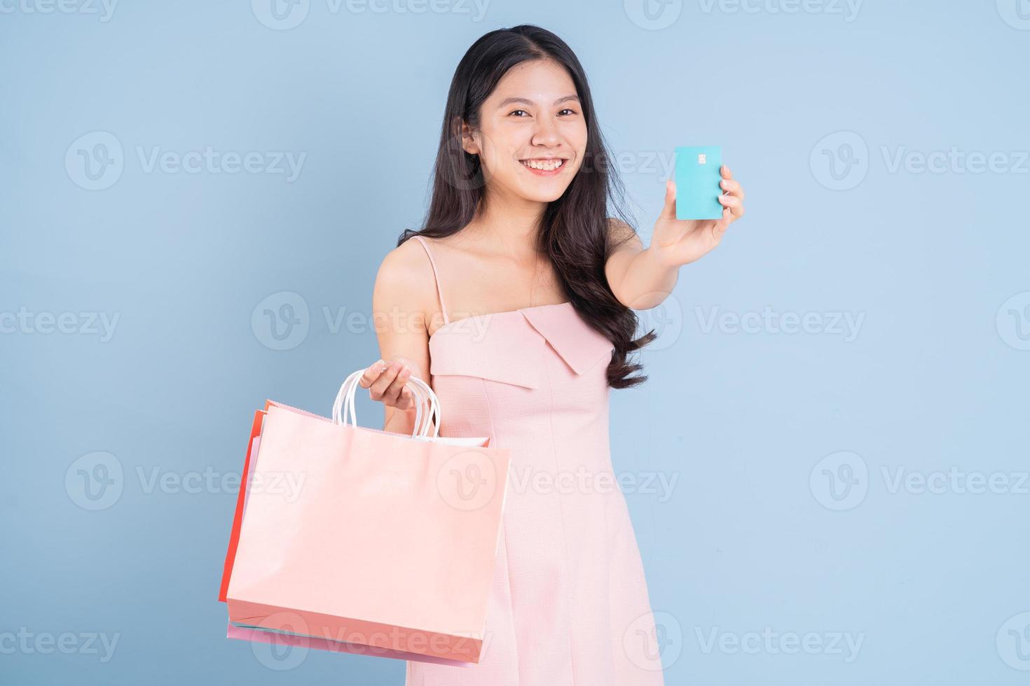 Beautiful young Asian woman holding shopping bag on blue background photo