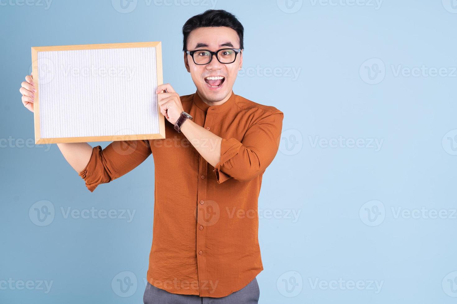 Young Asian man holding white board on blue background photo