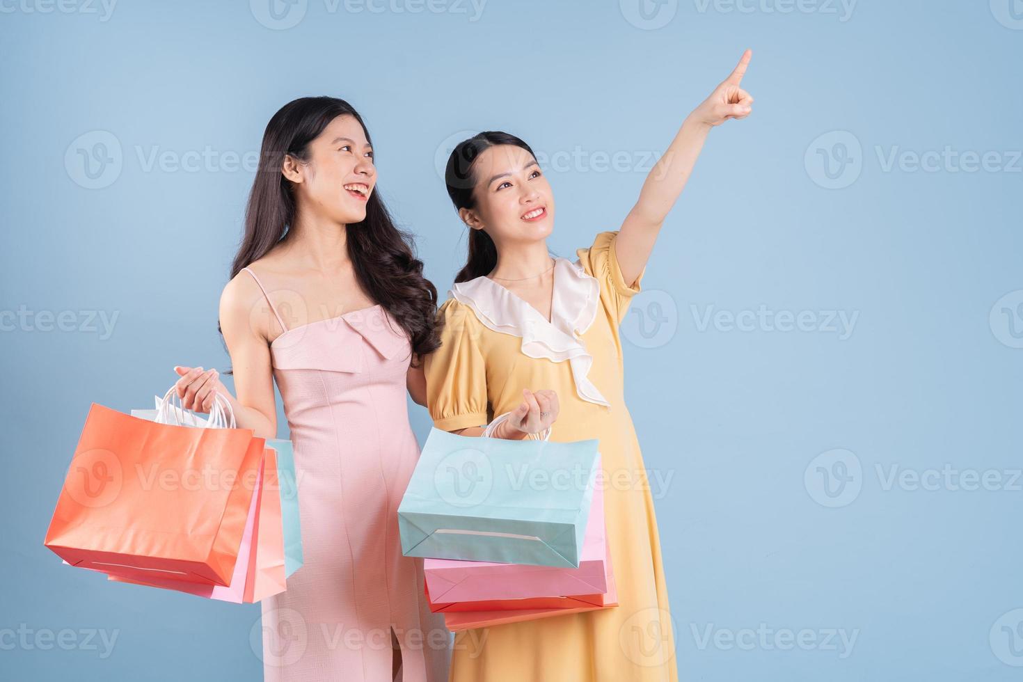 Dos jóvenes mujeres asiáticas sosteniendo una bolsa de compras sobre fondo azul. foto