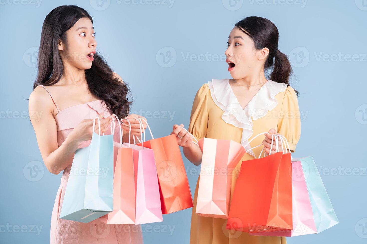 Dos jóvenes mujeres asiáticas sosteniendo una bolsa de compras sobre fondo azul. foto