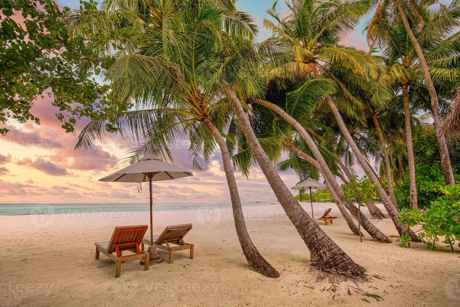 Romantic tropical sunset scenery, two sun beds, loungers, umbrella under palm tree. White sand, sea view with horizon, colorful twilight sky, calmness and relaxation. Inspirational beach resort hotel photo