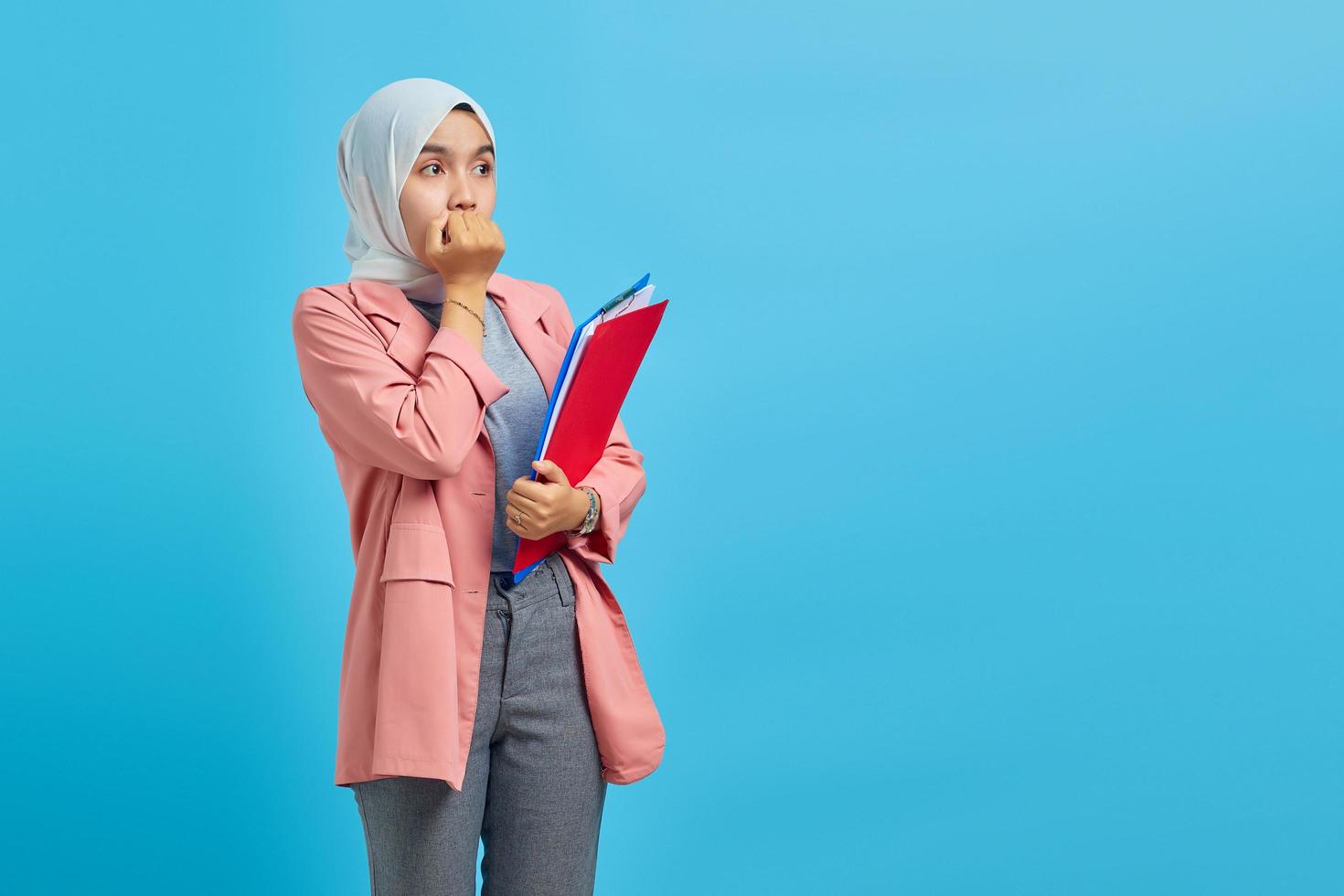 Surprised young Asian woman holding folder and looking at empty spaceover blue background photo