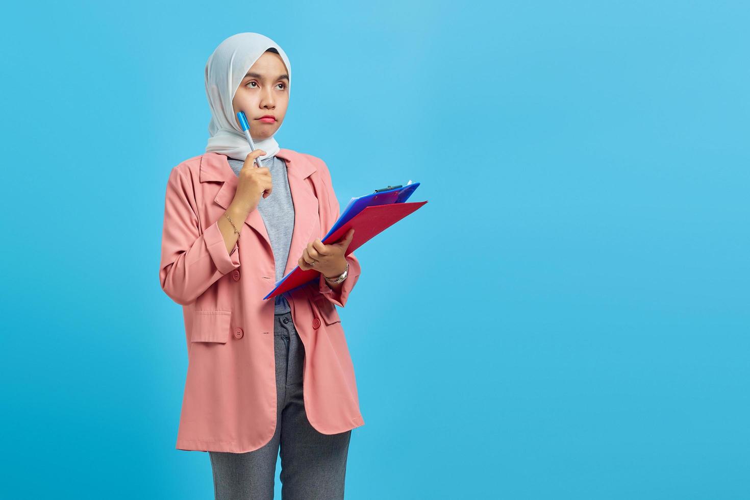 Joven mujer asiática concentrada escribiendo notas planificando la creación de estrategia sobre fondo azul. foto